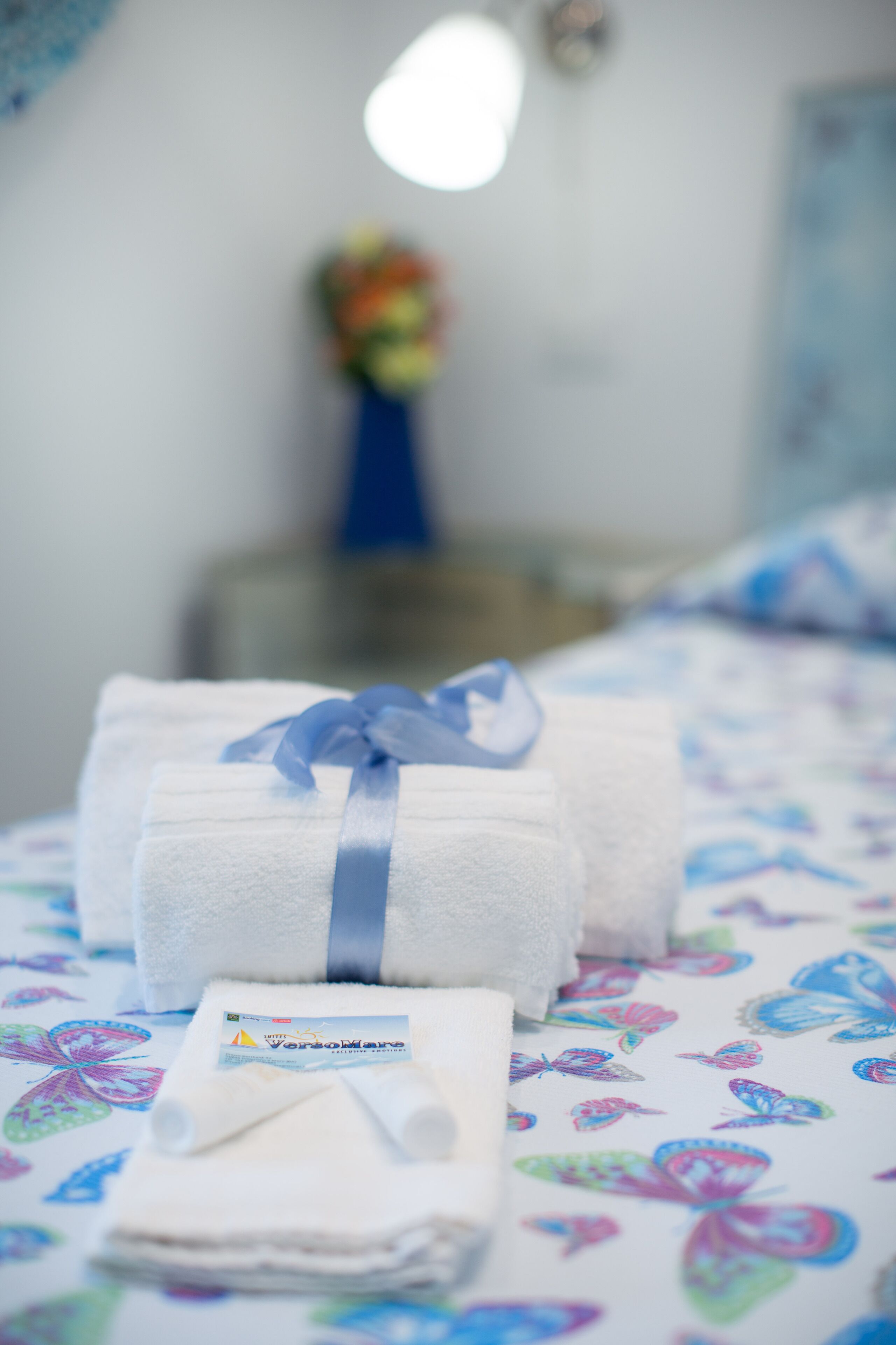 Strak opgevouwen witte handdoeken met een blauw lint op een bed met een kleurrijk vlindermotief.
