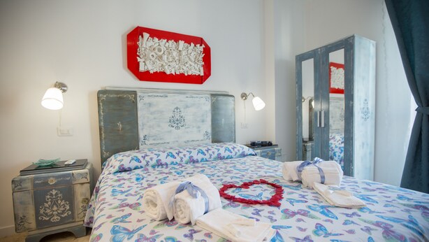A bedroom with a bed, a nightstand, a wardrobe, and a wall decoration. - Versomare - Room Grecale - extra Bed On Demand (Polignano A Mare)