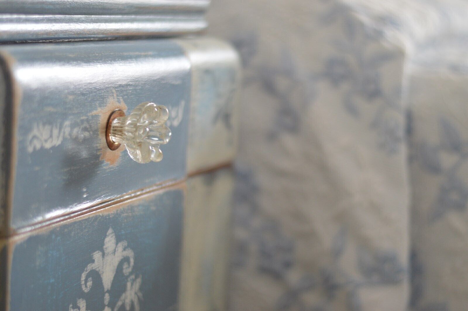 A close-up of a vintage dresser with a floral pattern and a clear glass knob.