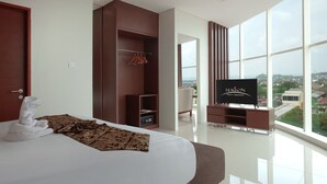 A modern hotel room with a large bed, a wardrobe, a television, and a view of the city. - Hotel Horison Nindya Semarang (Semarang)