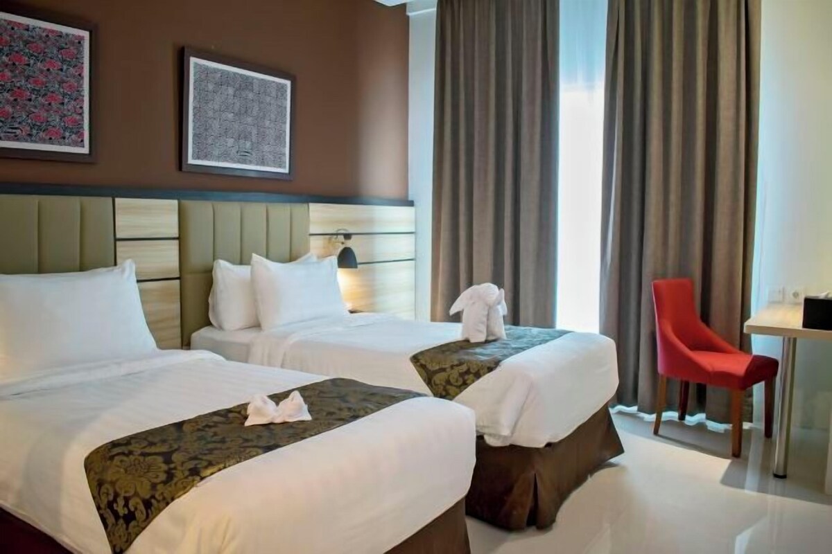 A hotel room with two beds, a red chair, a small table, and a large window with curtains.