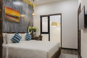 A bedroom with a bed, pillows, a painting, a plant, and a view through a door. - Caprice Hotel Danang (Da Nang)
