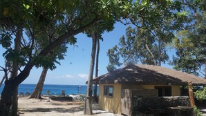 A beach house with a thatched roof, surrounded by trees and overlooking the ocean. - Vanuatu Uncharted Sport Fishing Lounge (Mele)