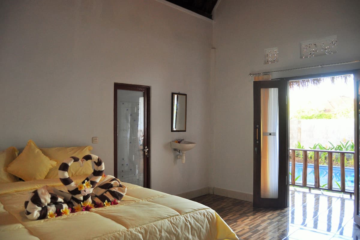 A hotel room with a bed, a bathroom mirror, a sink, and a view of a pool.