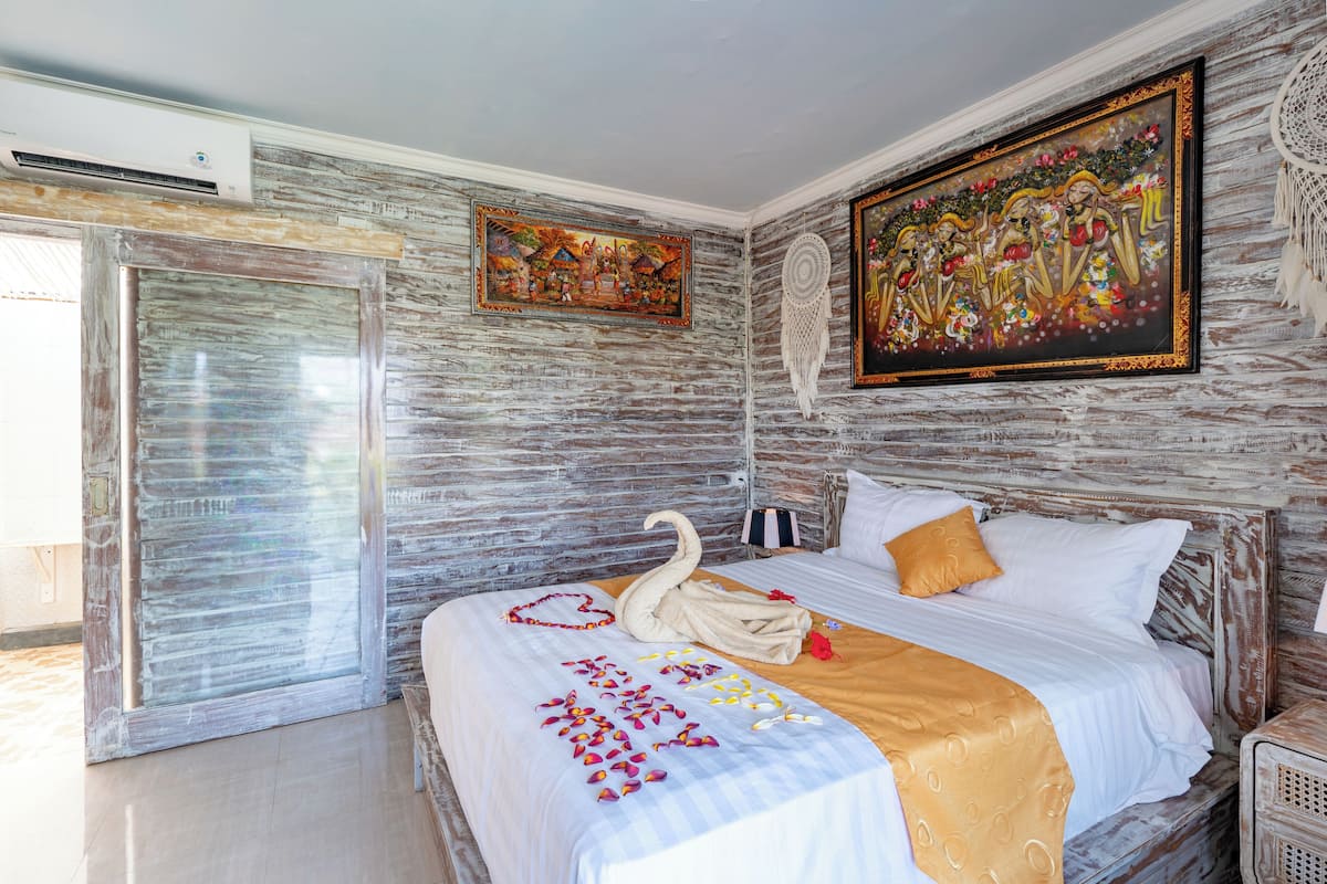 A bedroom with a bed, a wall-mounted air conditioner, and two paintings.