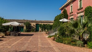 A courtyard with a tiled floor, outdoor seating, and a building with a green door and windows. - Charming nineteenth-century villa in Caltagirone (Caltagirone)