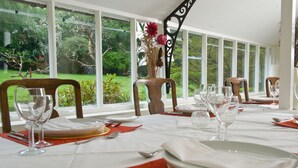 A dining area with a table set for a meal, large windows with a view of greenery, and a decorative vase with flowers. - Amazing New Forest location - Sleeps up to 14 people (Brockenhurst)