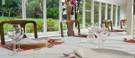 A dining area with a table set for a meal, large windows with a view of greenery, and a decorative vase with flowers.