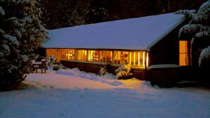 A snow-covered house with a lit interior, surrounded by snow and trees. - Amazing New Forest location - Sleeps up to 14 people (Brockenhurst)