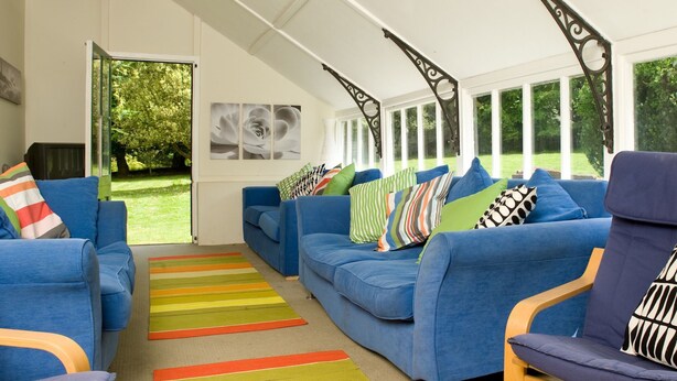 A spacious sunroom with a blue sofa set, colorful striped rugs, and a view of greenery outside. - Amazing New Forest location - Sleeps up to 14 people (Brockenhurst)