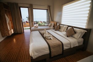 Habitación de hotel con una cama grande, piso de madera, vista al mar y un balcón con barandilla de madera.
