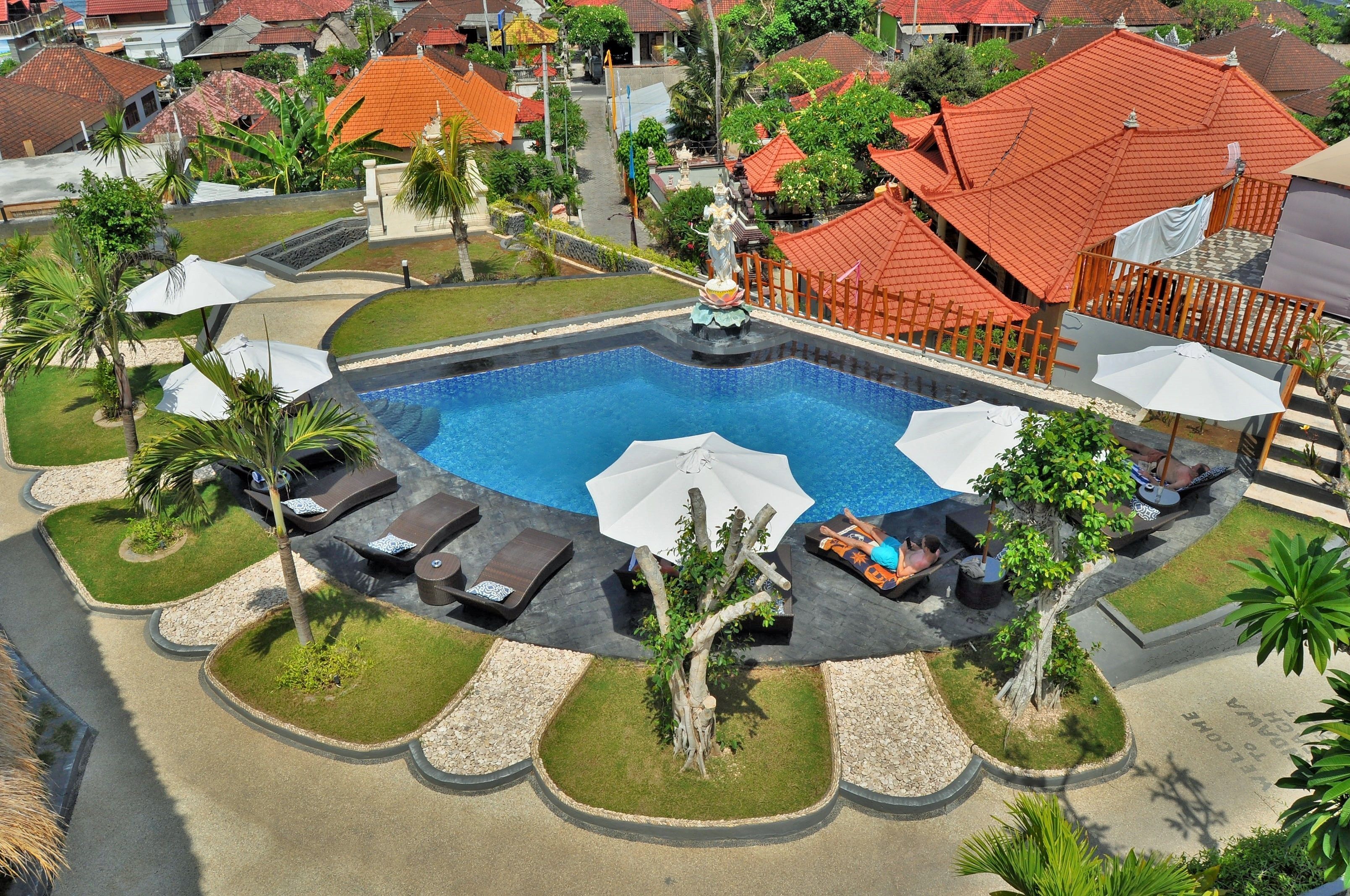 Piscina com espreguiçadeiras e guarda-sóis, cercada por palmeiras e um pequeno jardim.