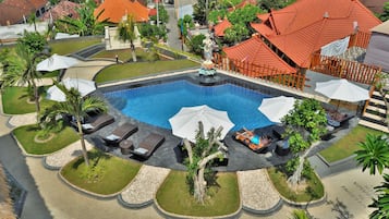 Piscina com espreguiçadeiras e guarda-sóis, cercada por palmeiras e um pequeno jardim.