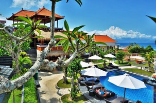Un resort con piscina, sillas de descanso, sombrillas y vistas al océano.