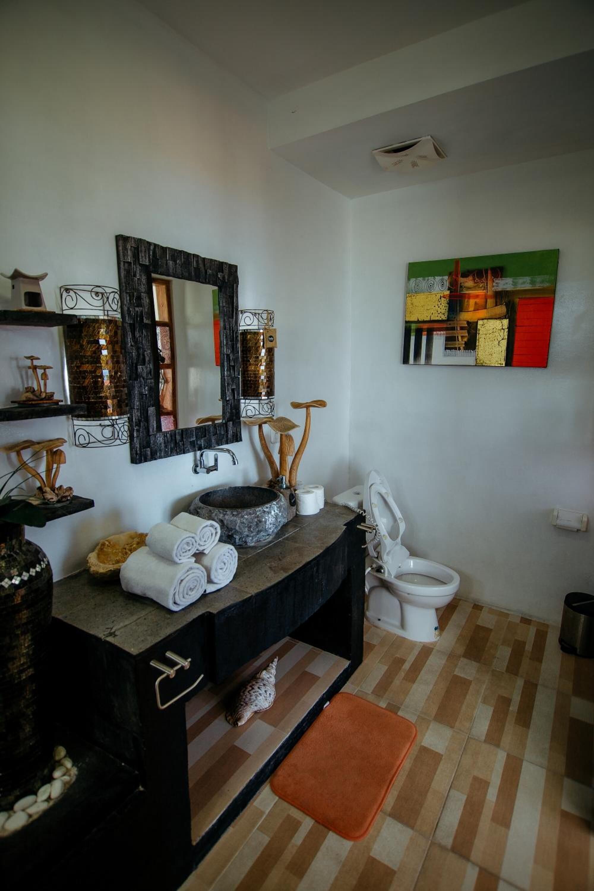 Un baño con tocador negro, un espejo grande, un inodoro blanco y un estante decorativo con toallas.