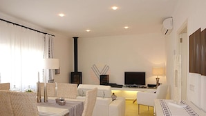 Una sala de estar moderna con comedor, chimenea, televisor de pantalla plana y un amplio ventanal con cortinas.