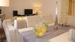 Una habitación de hotel moderna con sofá, televisión, lámpara y mesa de comedor con un jarrón de flores.