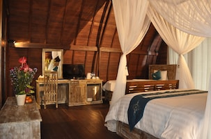 A bedroom with a wooden ceiling, a bed with white bedding, a wooden desk with a television, and a mirror.