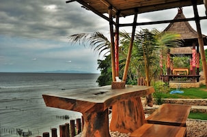 A wooden table and bench by the sea, a gazebo, and a small pool area.