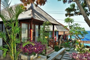 A beachfront property with a wooden house, a pool, and lush tropical plants.