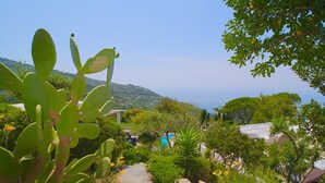 Un chemin de pierre mène à un espace piscine, entouré d’une végétation luxuriante et offrant une vue sur la mer.
