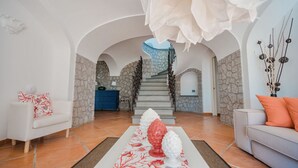 Un vaste espace de vie avec un escalier menant à un deuxième étage, des murs en pierre et un mobilier moderne.