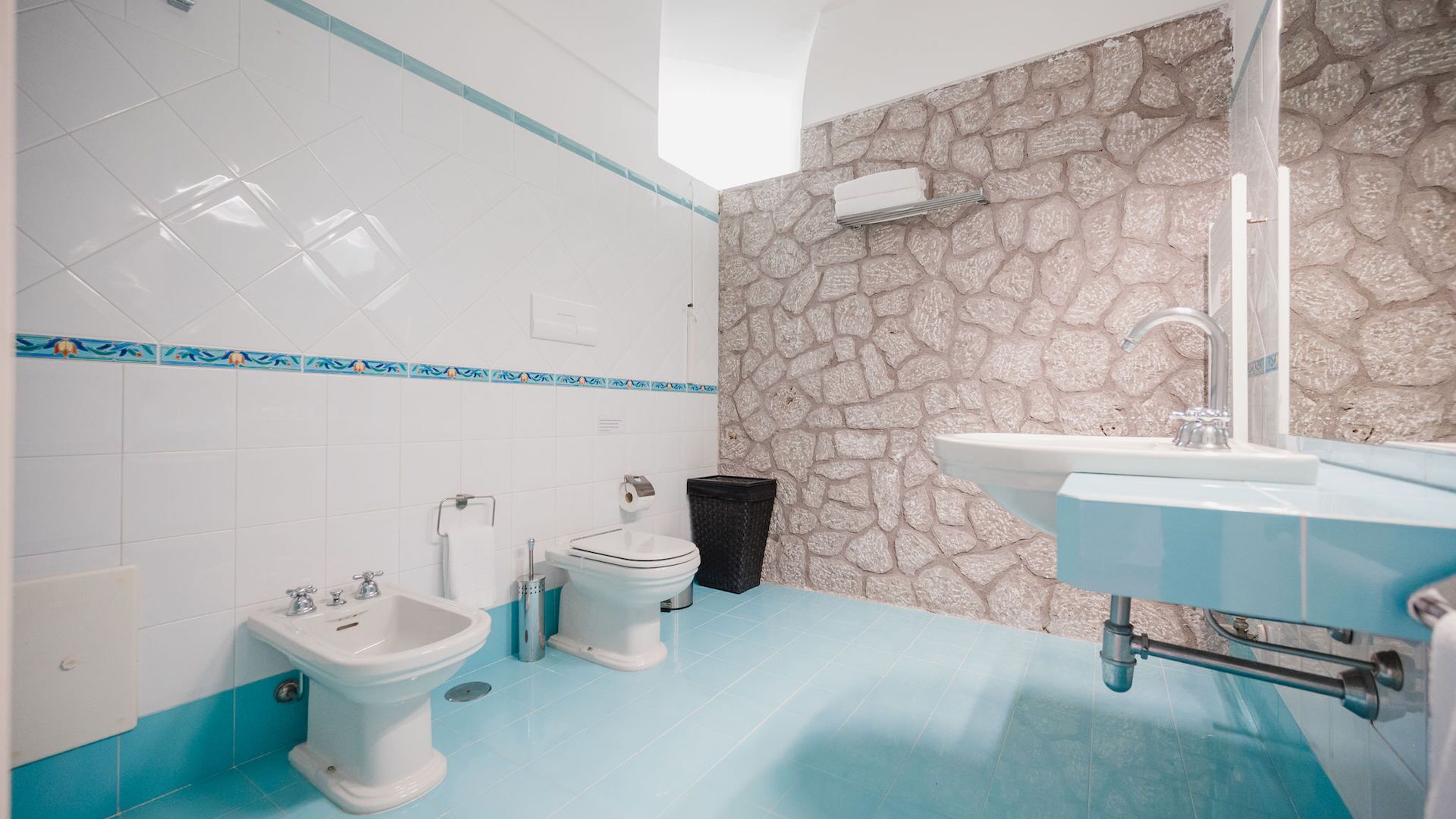 Un baño con una pared de acento de piedra, un lavabo blanco, un bidé y un inodoro.