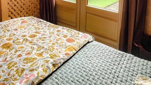 A bedroom with a bed, a window, and a view of an outdoor patio. - Chalet-style apartment—3 rooms, 2 bedrooms, ground floor, small garden, parking—3 minutes from the base of the slopes, near the center (La Clusaz)
