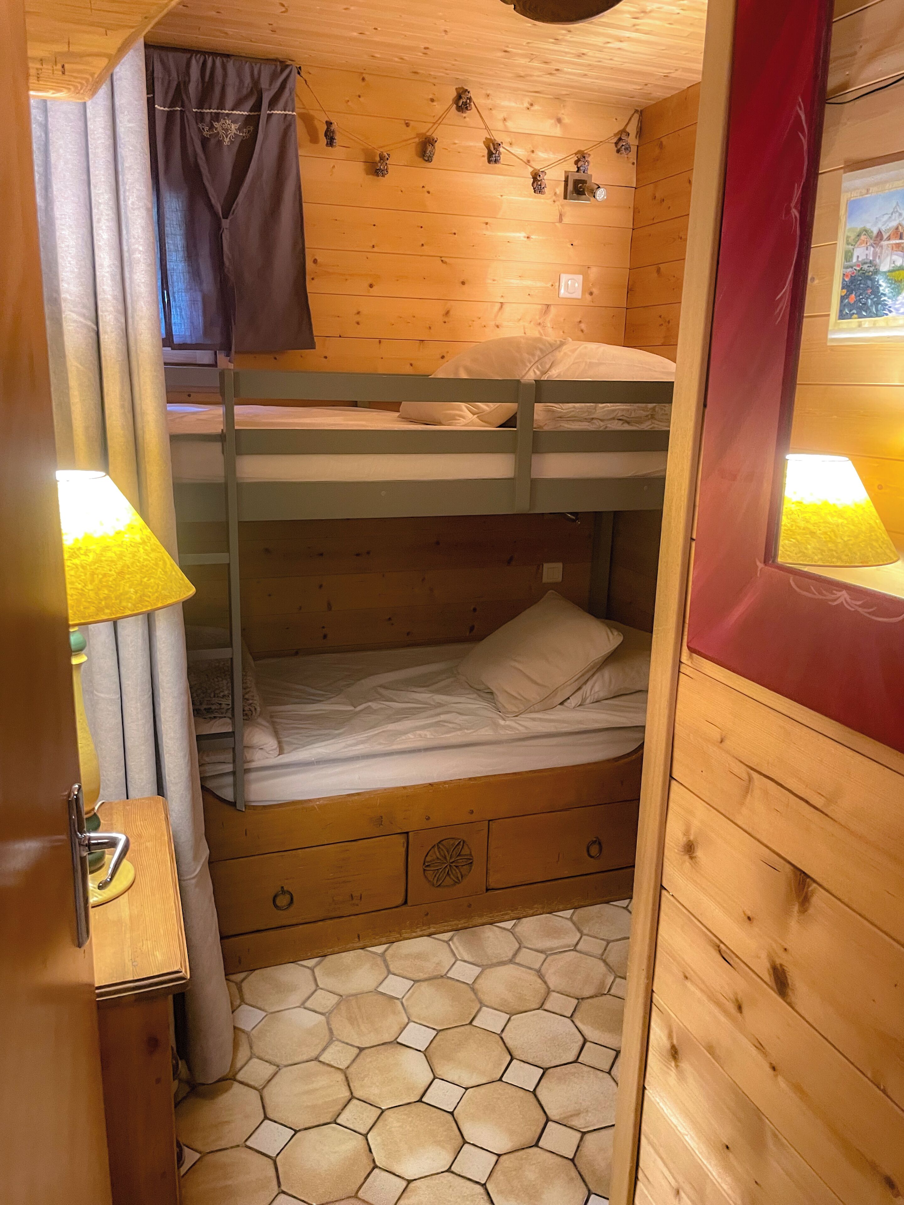 Ein Schlafraum mit Etagenbetten, Holzboden, einem kleinen Schreibtisch mit Lampe und einem hexagonalen Fußboden.