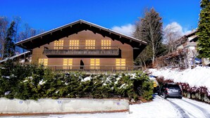 A chalet-style building with a wooden facade, balconies, and a snow-covered landscape. - Chalet-style apartment—3 rooms, 2 bedrooms, ground floor, small garden, parking—3 minutes from the base of the slopes, near the center (La Clusaz)