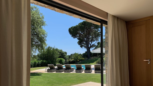 A room with a large sliding glass door leading to a pool area with lounge chairs and a well-maintained lawn. - Luxury, modern villa, 8min walking distance to town and beaches - heated pool (Sainte-Maxime)