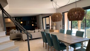 A modern living room with a staircase, a dining area with a wooden table and teal chairs, and a kitchen area with a TV and shelves. - Luxury, modern villa, 8min walking distance to town and beaches - heated pool (Sainte-Maxime)