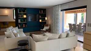 A modern living room with a large flat-screen TV, a sofa, a coffee table, and a bookshelf. - Luxury, modern villa, 8min walking distance to town and beaches - heated pool (Sainte-Maxime)