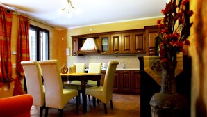 Uma área de refeições com uma mesa e cadeiras, uma cozinha ao fundo e um vaso com flores sobre uma mesa.