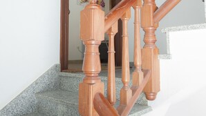 Un escalier en bois, doté d’une rampe, mène à une pièce qui possède une porte et un interrupteur sur le mur.