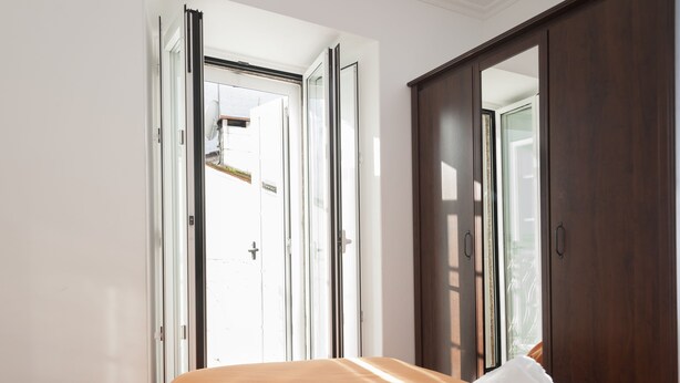 Une chambre avec une porte ouverte donnant sur l’extérieur, un lit recouvert d’une couverture orange et un grand miroir accroché au mur.