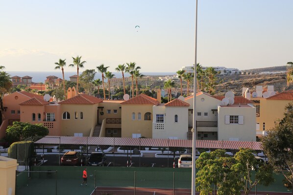 A coastal resort with Mediterranean-style buildings, a tennis court, and a view of the sea.