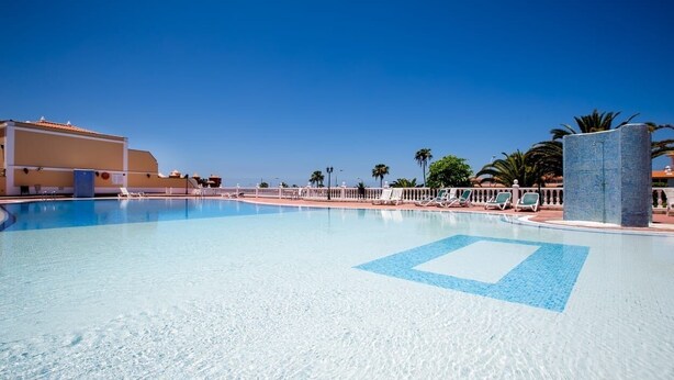 A clear blue swimming pool with lounge chairs and palm trees in the background. - El Veril Duque, 2 bed apartment, sleeps 4, only 7 min walk to El Duque beach (Costa Adeje)