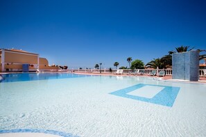A clear blue swimming pool with lounge chairs and palm trees in the background.