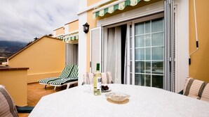 A terrace with a table set for dining, striped lounge chairs, and a bottle of wine. - El Veril Duque, 2 bed apartment, sleeps 4, only 7 min walk to El Duque beach (Costa Adeje)