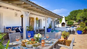 An outdoor dining area with a long wooden table set for a meal, surrounded by blue cushioned chairs. - Cozy family-friendly holiday home with many extras (Sao Bras de Alportel)