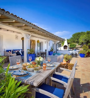 An outdoor dining area with a long wooden table set for a meal, surrounded by blue cushioned chairs. - Cozy family-friendly holiday home with many extras (Sao Bras de Alportel)