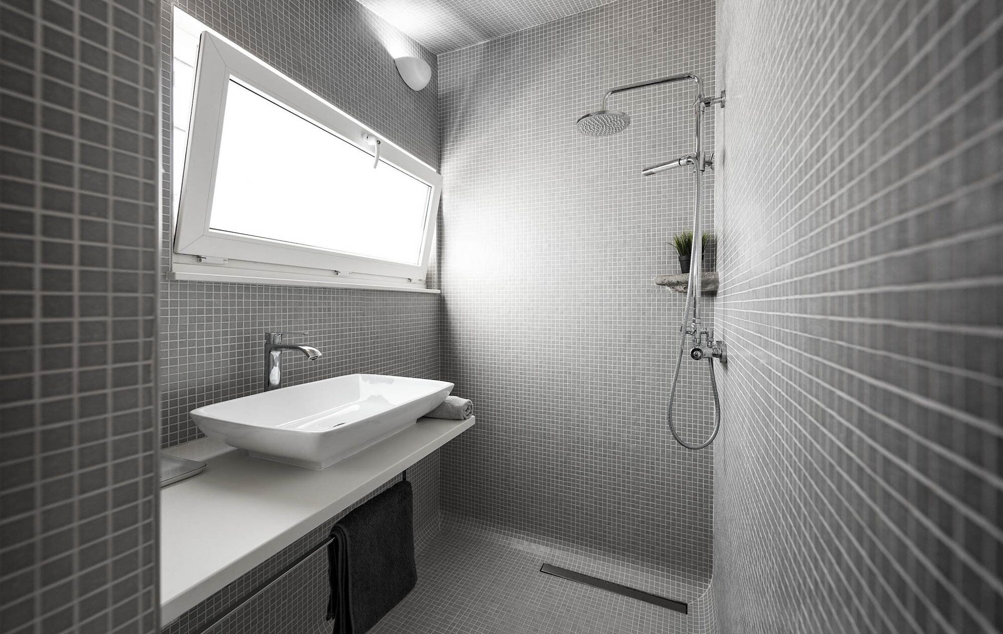 A modern bathroom with a large rectangular sink, a handheld showerhead, and a small window above the mirror.