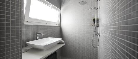 A modern bathroom with a large rectangular sink, a handheld showerhead, and a small window above the mirror.
