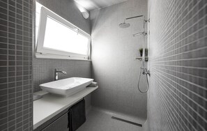 A modern bathroom with a large rectangular sink, a handheld showerhead, and a small window above the mirror.