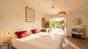 A bedroom with a large bed, a ceiling fan, a framed artwork, a bedside table with a lamp, and a view of the outdoors through a glass door. - Cozy family-friendly holiday home with many extras (Sao Bras de Alportel)
