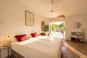 A bedroom with a large bed, a ceiling fan, a framed artwork, a bedside table with a lamp, and a view of the outdoors through a glass door. - Cozy family-friendly holiday home with many extras (Sao Bras de Alportel)