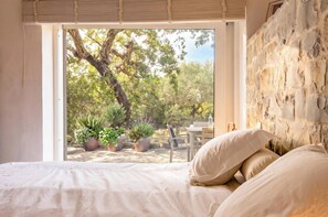 A bedroom with a large window, a bed with white linens, and a stone wall. - Cozy family-friendly holiday home with many extras (Sao Bras de Alportel)