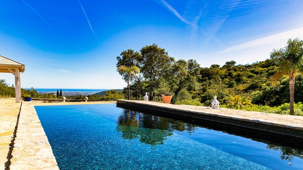A clear blue pool with a stone deck, surrounded by lush greenery and a view of the sea. - Cozy family-friendly holiday home with many extras (Sao Bras de Alportel)