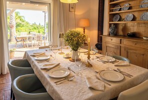 A dining table set for four with a vase of flowers, candles, and a view of the outdoors.